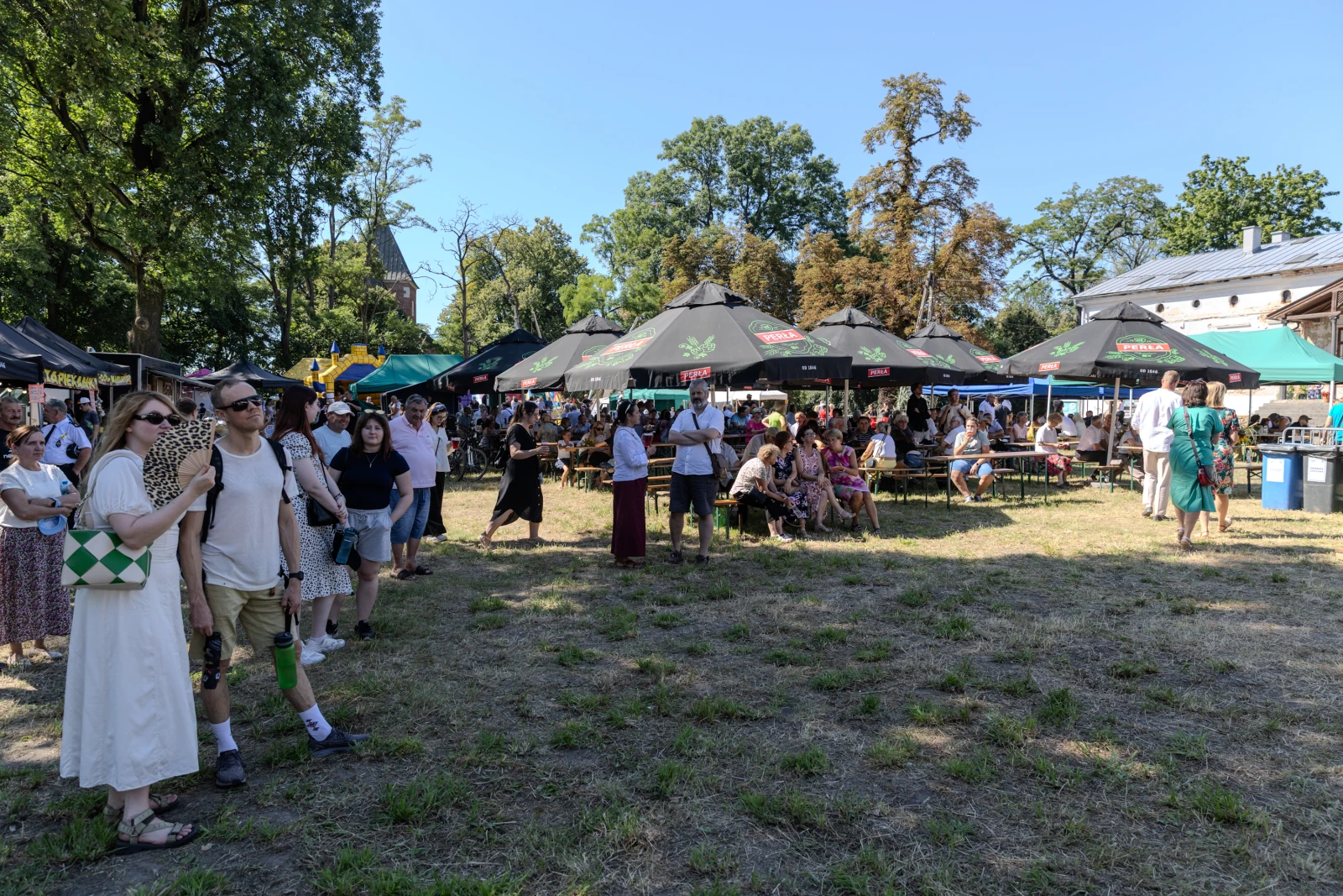 Tłum ludzi na festiwalu, stoiska z parasolami, zieleń wokół.  Autor: Bogusław Świerzowski