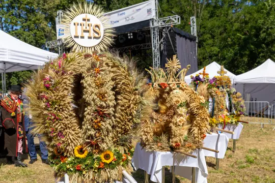 Wieniec dożynkowy ozdobiony kwiatami i zbożem, z napisem IHS na górze.