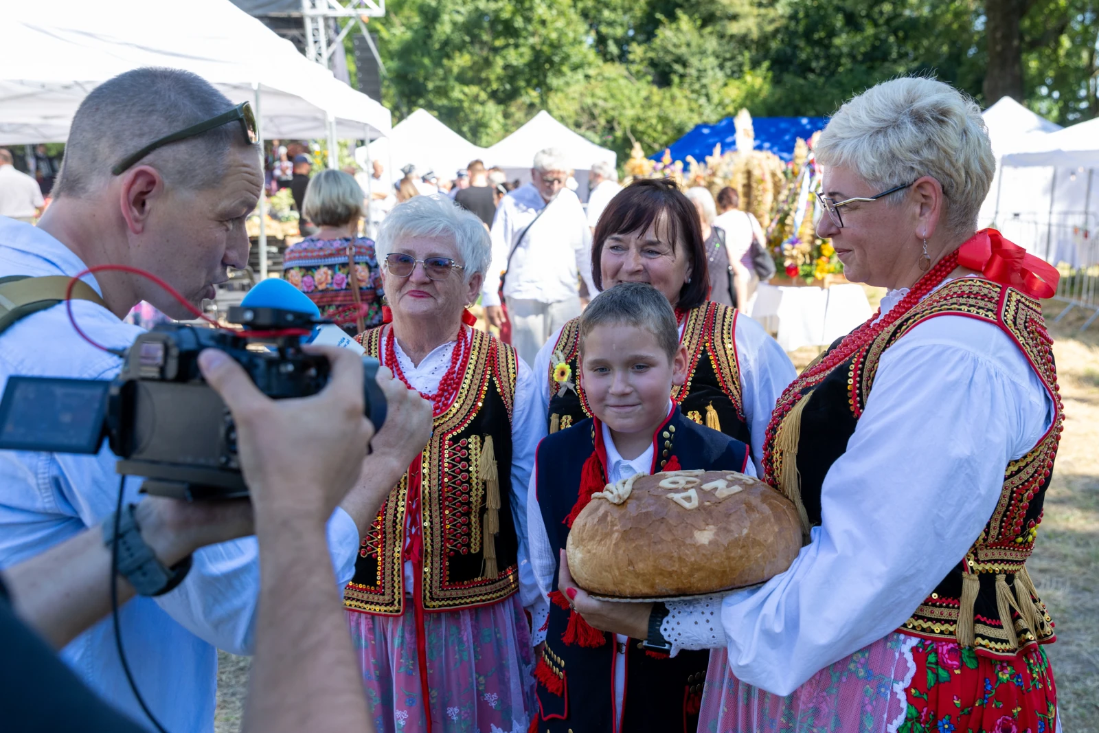 Grupa osób w tradycyjnych strojach ludowych trzyma chleb na festynie.  Autor: Bogusław Świerzowski