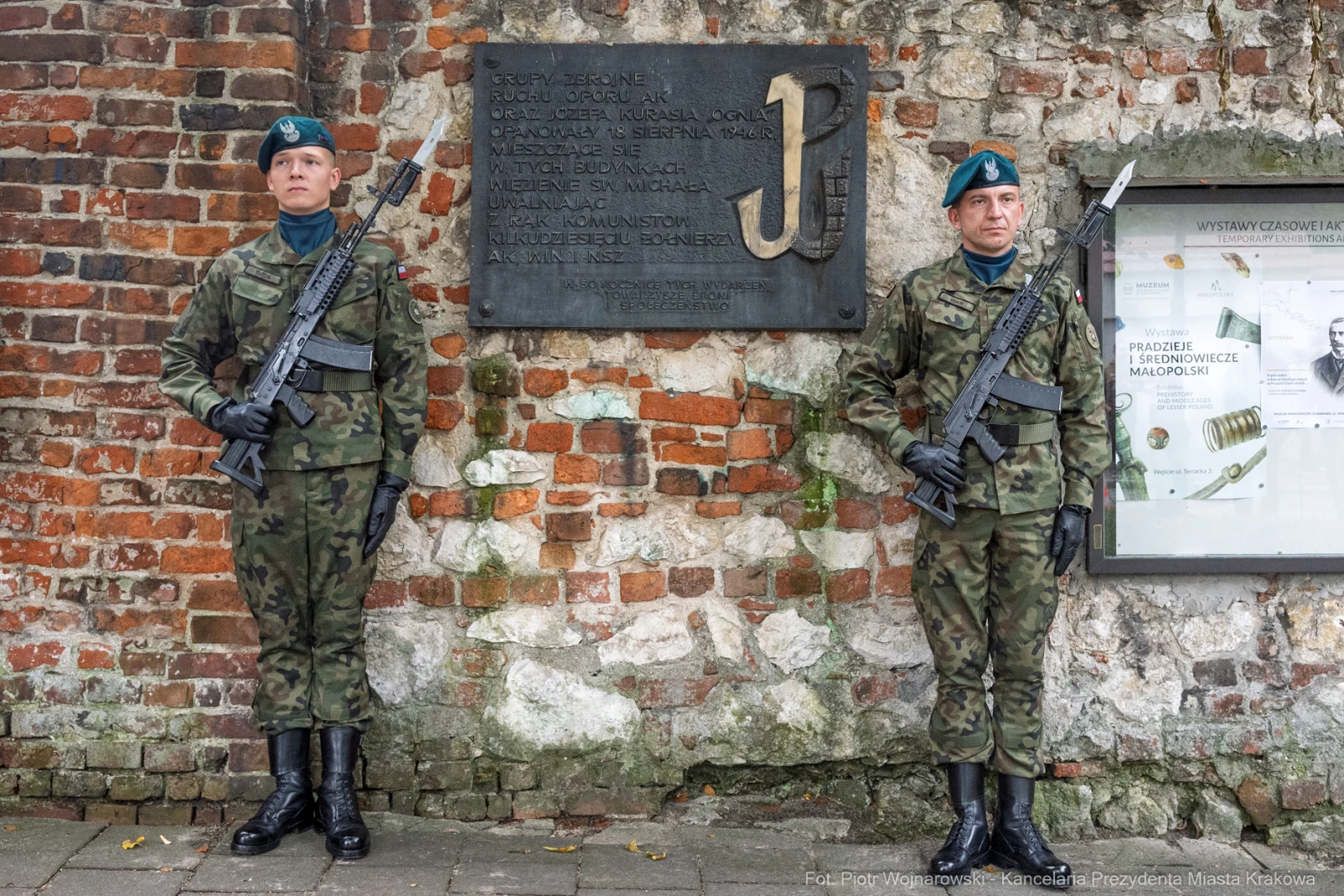 Dwaj żołnierze w mundurach z bronią, stojący przy tablicy pamiątkowej.  Autor: Piotr Wojnarowski