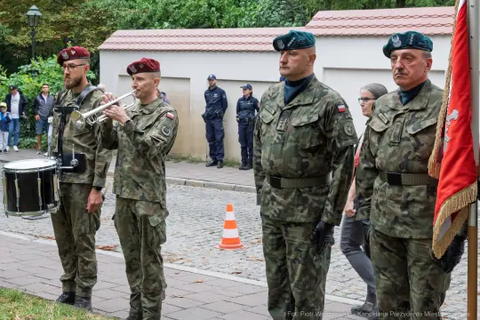 Żołnierze w mundurach wojskowych podczas ceremonii, grający na trąbce i bębnie.