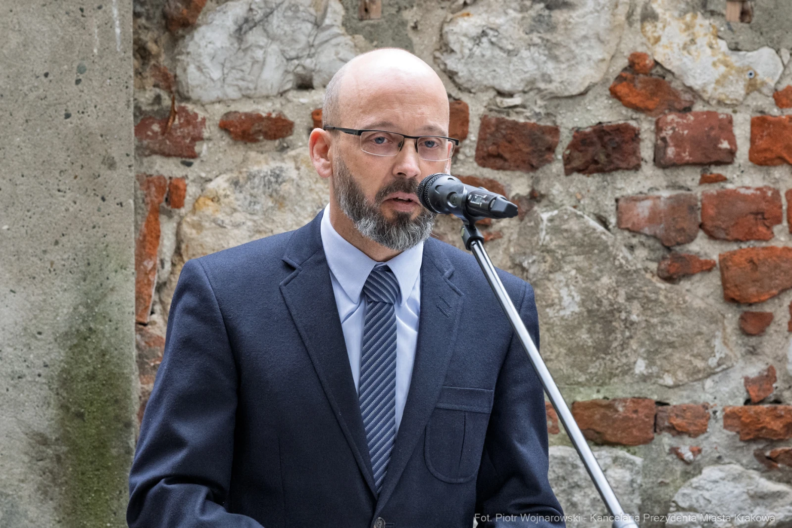 Mężczyzna w okularach przemawia do mikrofonu, w tle ceglana ściana.  Autor: Piotr Wojnarowski