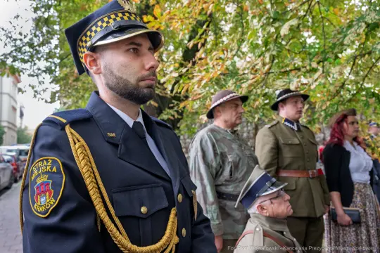 Mężczyzna w mundurze straży miejskiej oraz grupa osób w strojach historycznych.