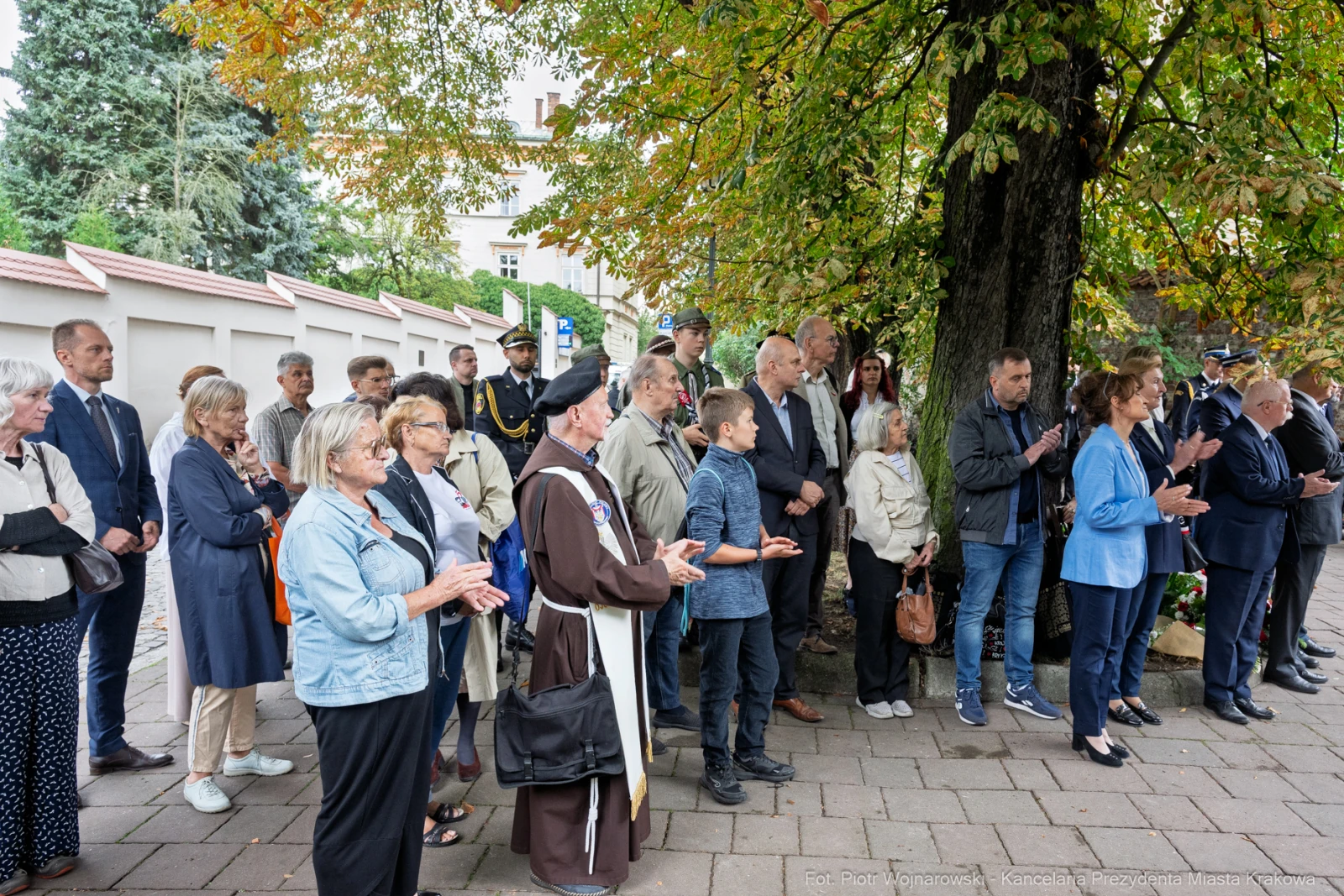 Grupa ludzi w różnym wieku, w tym duchowny, zgromadzona pod drzewem.  Autor: Piotr Wojnarowski