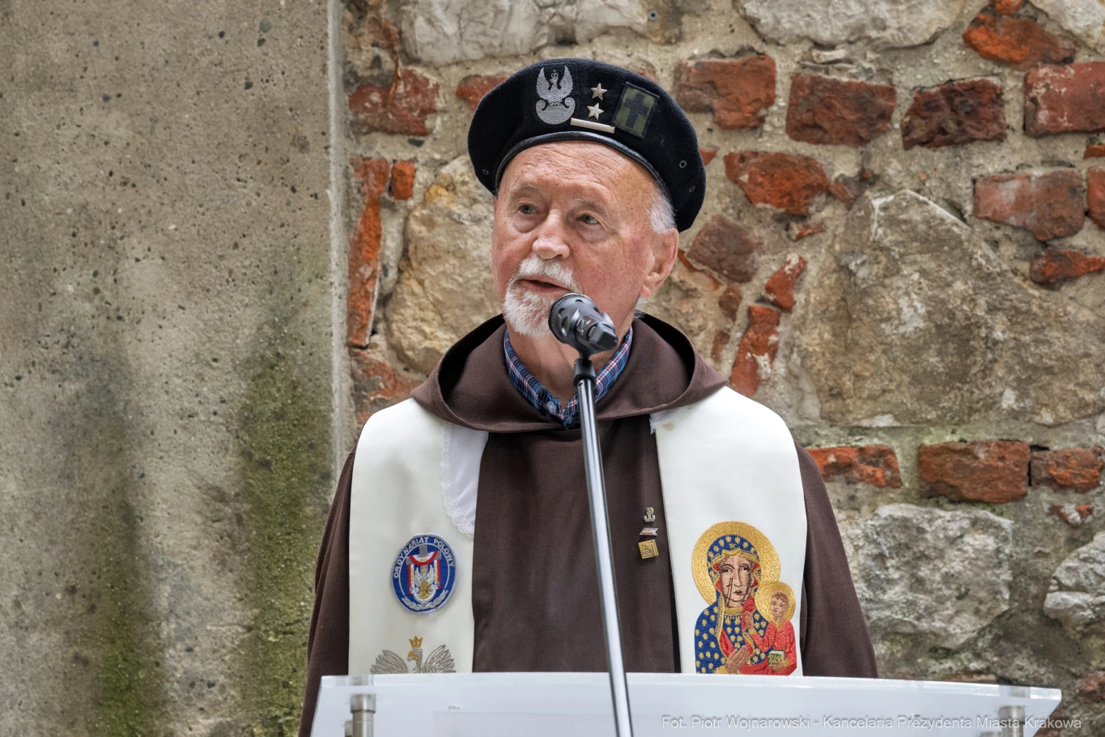 Mężczyzna w habicie z mikrofonem, z emblematami i ikoną na szatach, przemawia w historycznym otoczeniu.  Autor: Piotr Wojnarowski