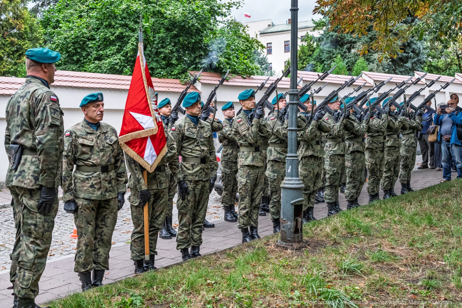 Żołnierze w mundurach wojskowych z bronią w ręku, salutujący z flagą.  Autor: Piotr Wojnarowski