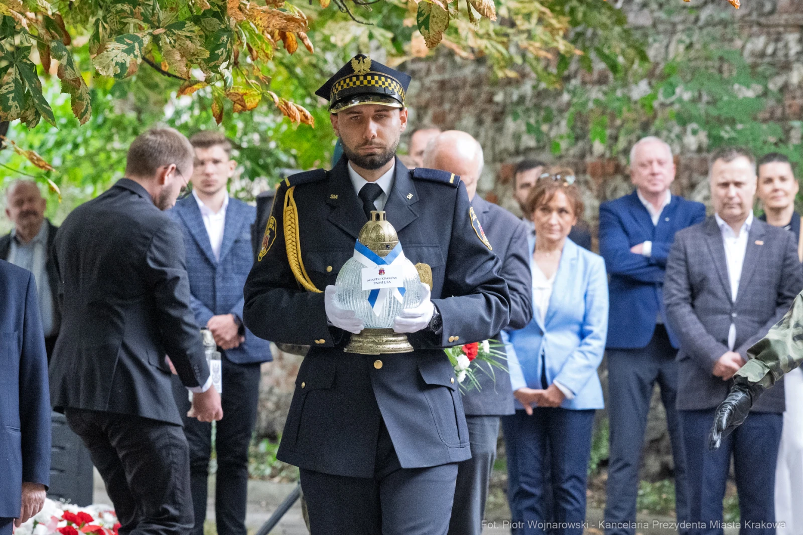 Mężczyzna w mundurze trzyma znicz, wokół zgromadzenie ludzi w tle.  Autor: Piotr Wojnarowski