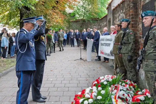 Uroczystość złożenia kwiatów w hołdzie bohaterom, obecność wojskowych i cywilów.