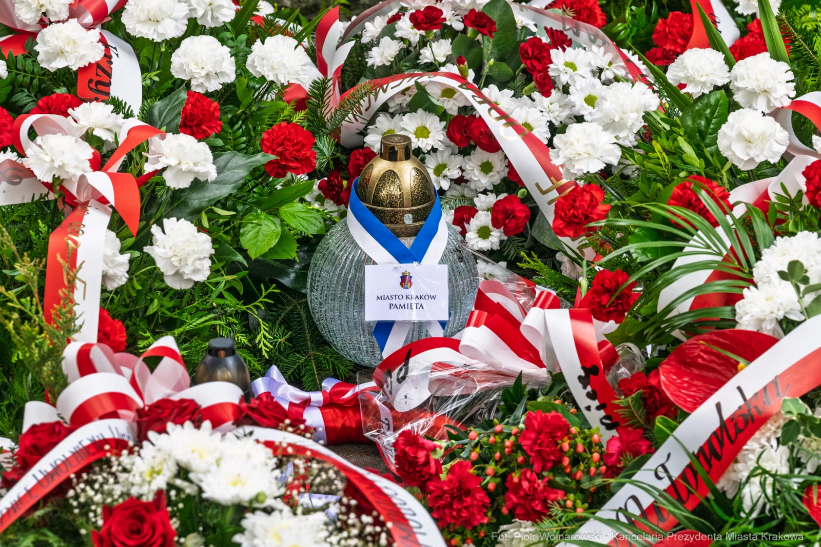 Wieniec z kwiatów w czerwonych i białych kolorach oraz znicz z napisem.  Autor: Piotr Wojnarowski