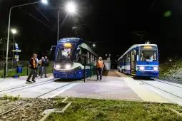 Dwa tramwaje na stacji w nocy, pasażerowie i pracownicy w odblaskowych kamizelkach.