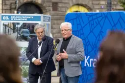 Dwóch mężczyzn przemawia na tle plansz z informacjami o projektach w Krakowie.