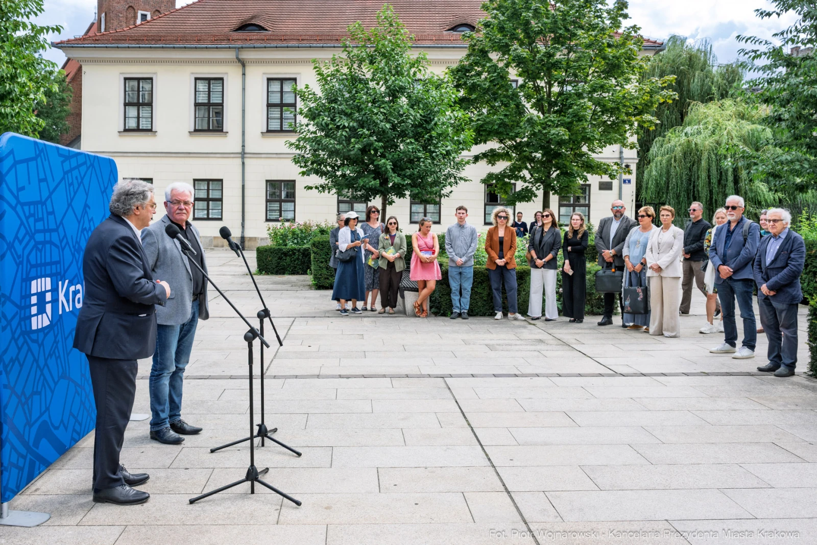 Dwaj mężczyźni przemawiają na tle grupy ludzi w parku.  Autor: Piotr Wojnarowski