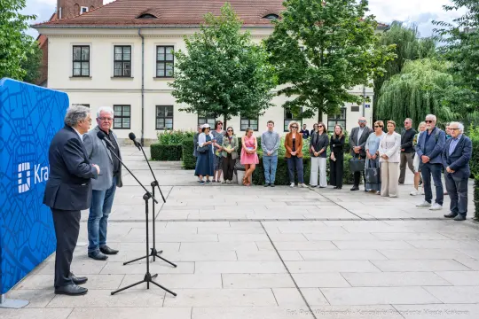 Dwaj mężczyźni przemawiają na tle grupy ludzi w parku.