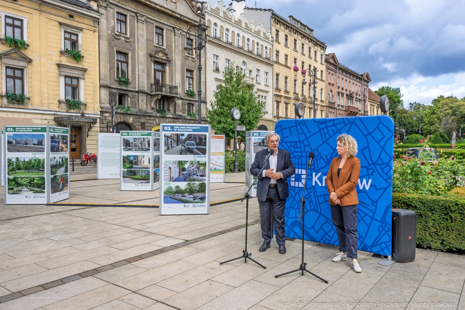Dwójka ludzi przy mikrofonach na tle plansz informacyjnych i miejskiego krajobrazu.  Autor: Piotr Wojnarowski