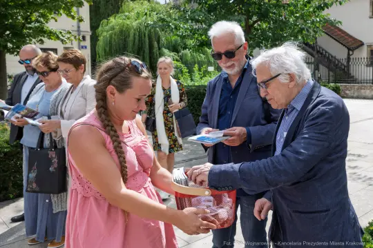 Kobieta wrzuca coś do koszyka, w tle grupa osób rozmawia i trzyma ulotki.