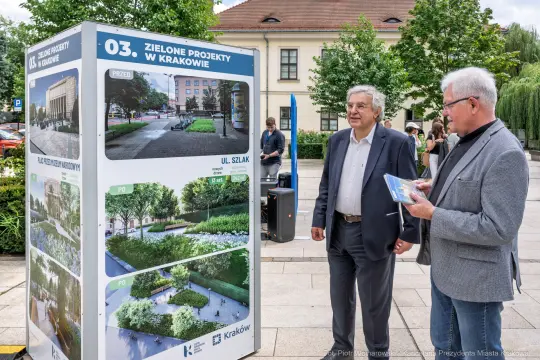 Mężczyźni oglądają planszę z zielonymi projektami w Krakowie.
