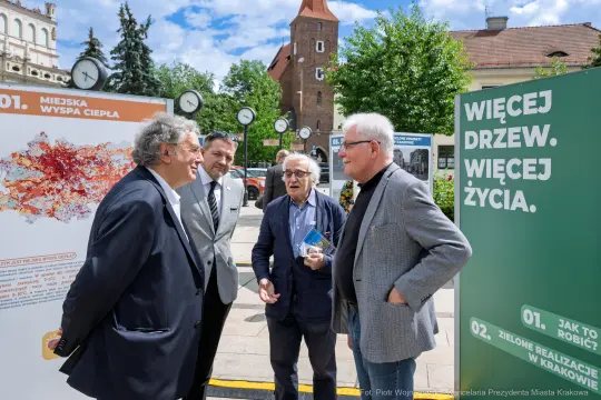 Czterech mężczyzn rozmawia na tle plakatów o miejskich projektach w Krakowie.