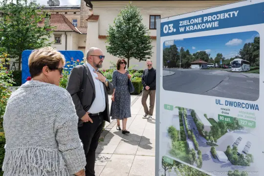 Grupa osób przy tablicy informacyjnej o zielonych projektach w Krakowie.