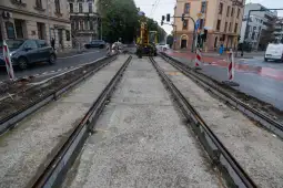 Remont torowiska tramwajowego na ulicy, widoczne maszyny budowlane i znaki drogowe.