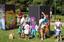 Grupa dzieci i dorosłych maluje kolorowe graffiti na panelach w parku.
