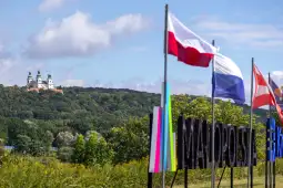 Widok na wzgórze z kościołem i flagami, w tle zielone drzewa i niebo.