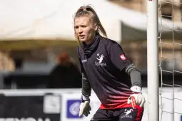 Kobieta bramkarka w stroju sportowym, przygotowująca się do obrony w meczu piłki nożnej.