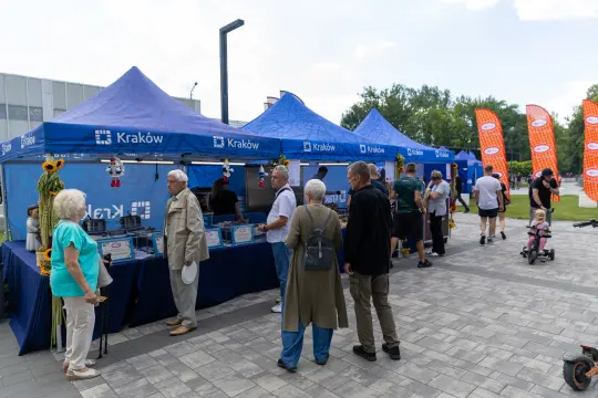 Stoiska z informacjami w Krakowie, ludzie rozmawiają i odbierają materiały.