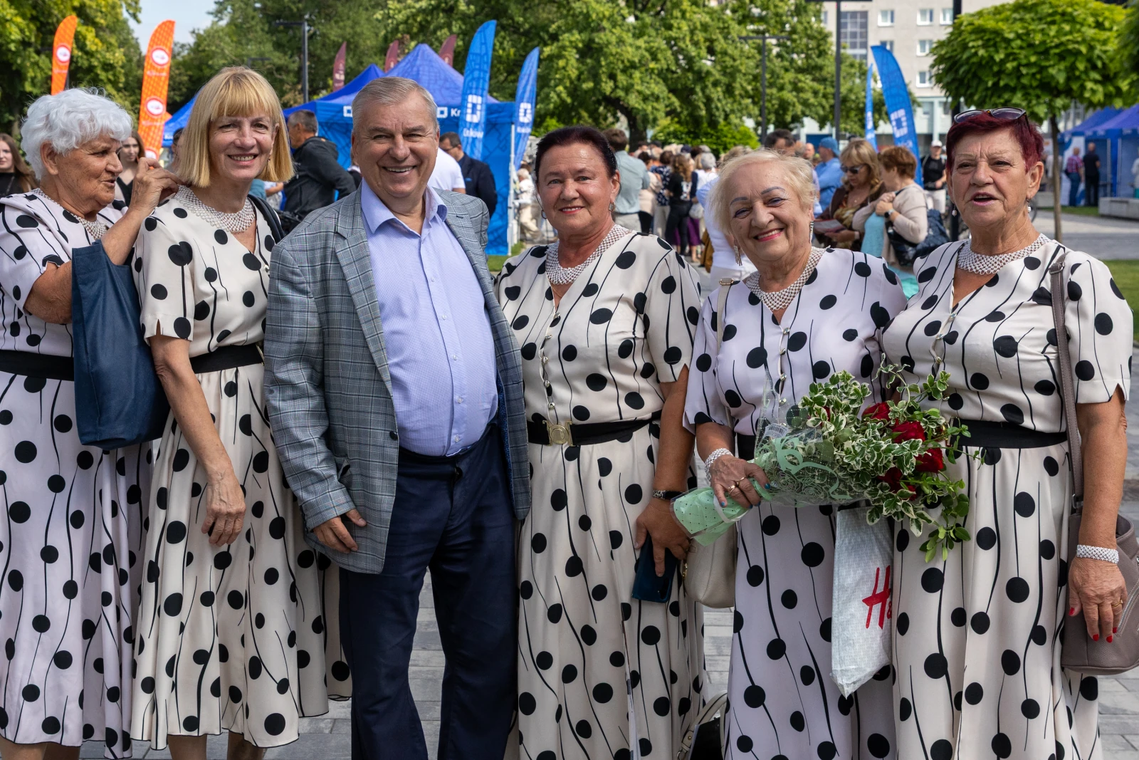 Grupa kobiet w sukienkach w kropki pozująca z mężczyzną na tle festiwalu.  Autor: Bogusław Świerzowski