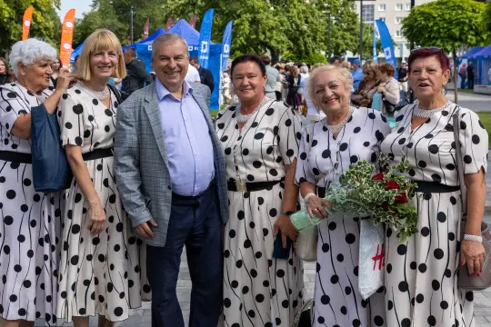 Grupa kobiet w sukienkach w kropki pozująca z mężczyzną na tle festiwalu.