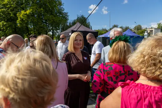 Kobieta w brązowej sukience wśród grupy ludzi na wydarzeniu plenerowym.