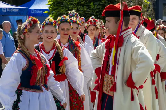 Grupa osób w tradycyjnych strojach ludowych, tańczących i świętujących na festiwalu.