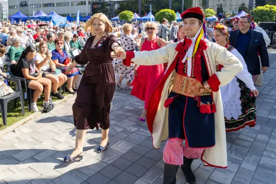 Parada w tradycyjnych strojach, uczestnicy tańczą i bawią się na festiwalu.