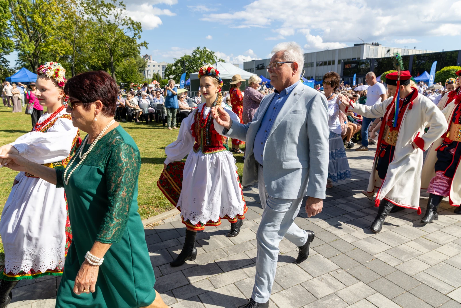 Grupa osób w tradycyjnych strojach ludowych tańczy i uczestniczy w wydarzeniu kulturalnym.  Autor: Bogusław Świerzowski