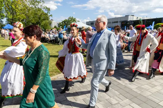 Grupa osób w tradycyjnych strojach ludowych tańczy i uczestniczy w wydarzeniu kulturalnym.