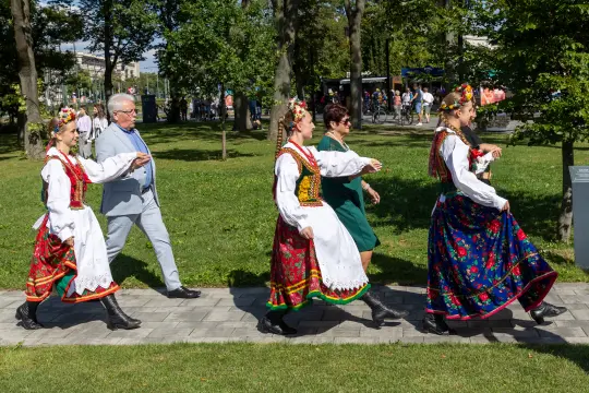 Grupa osób w tradycyjnych strojach ludowych spaceruje po parku.