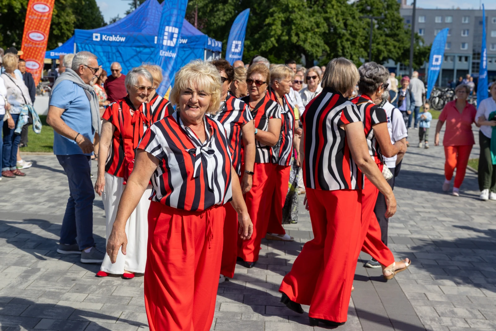 Grupa kobiet w czerwonych spodniach i pasiastej odzieży tańczy na ulicy w słoneczny dzień.  Autor: Bogusław Świerzowski