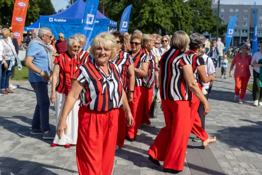 Grupa kobiet w czerwonych spodniach i pasiastej odzieży tańczy na ulicy w słoneczny dzień.