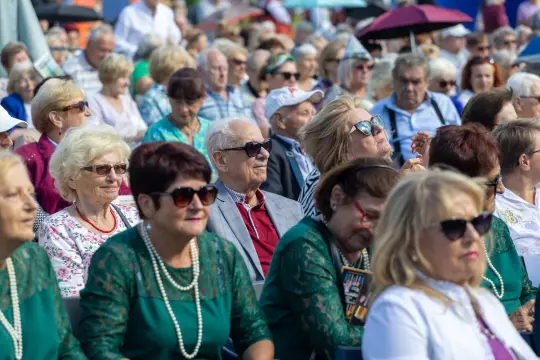 Tłum ludzi w okularach przeciwsłonecznych, siedzących na widowni podczas wydarzenia plenerowego.