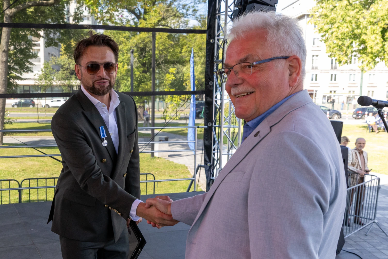 Dwaj mężczyźni uścisnęli sobie dłonie na tle sceny.  Autor: Bogusław Świerzowski