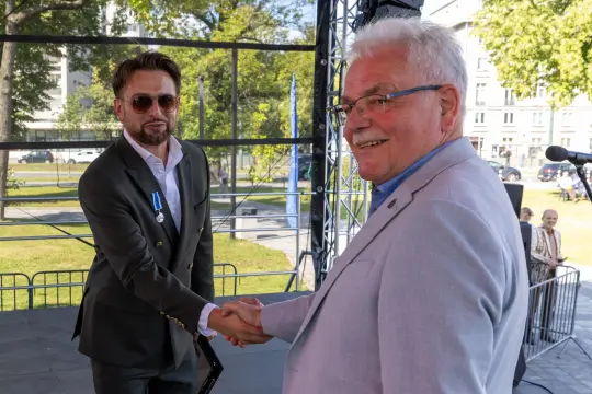 Dwaj mężczyźni uścisnęli sobie dłonie na tle sceny.