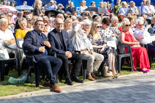 Grupa ludzi siedzących na krzesłach podczas wydarzenia na świeżym powietrzu.