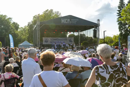 Tłum ludzi na wydarzeniu kulturalnym, scena z występami, słoneczna pogoda.