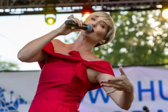 Kobieta w czerwonej sukience śpiewa do mikrofonu na scenie.