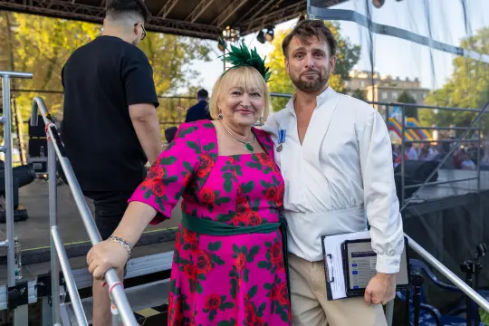 Kobieta w kwiecistej sukience i mężczyzna w białej koszuli na tle sceny.