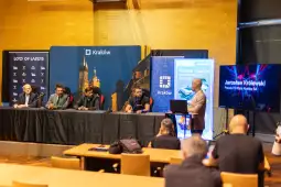 Konferencja prasowa w Krakowie z udziałem kilku mężczyzn przy stole oraz prezentacją na ekranie.