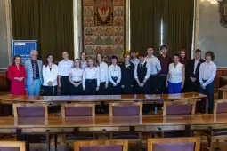 Grupa uczniów i nauczycieli w sali z dekoracjami na ścianach.