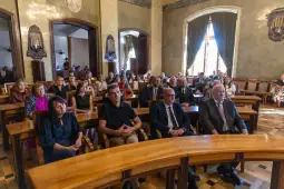 Grupa ludzi siedzących w sali, uczestniczących w wydarzeniu formalnym.