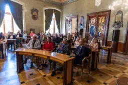 Grupa osób siedzących w sali konferencyjnej, uczestniczących w spotkaniu.