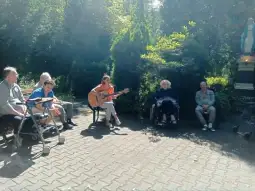 Osoby starsze słuchające muzyki na świeżym powietrzu, jedna gra na gitarze.