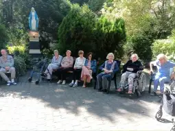 Grupa osób starszych siedzących na zewnątrz w otoczeniu zieleni.